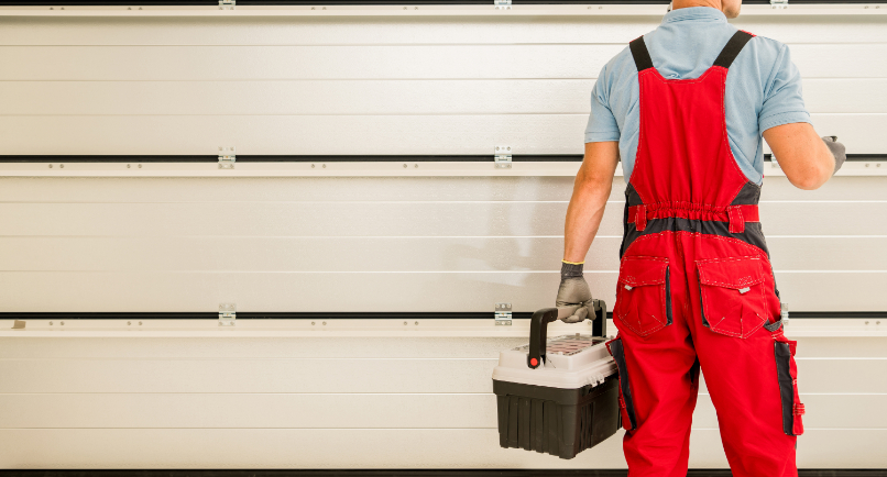 A person wearing red overalls and gloves stands in front of a closed garage door, holding a black toolbox—ready for a Garage Door Repair Plant City FL job, their back turned to the camera.